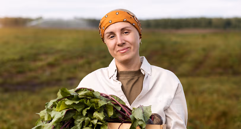 Person with orange bandana holding a crate of fresh green leafy vegetables outdoors.